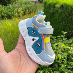 Child's shoe with a cartoon face design held in front of green foliage