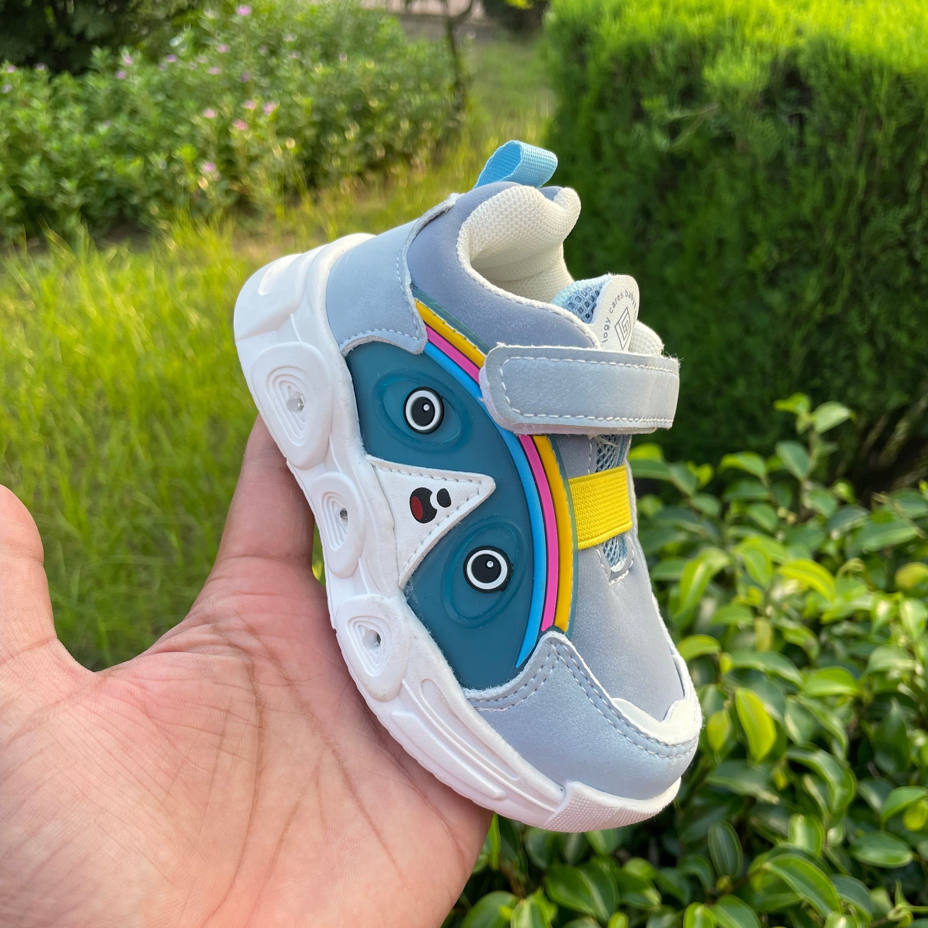 Child's shoe with a cartoon face design held in front of green foliage